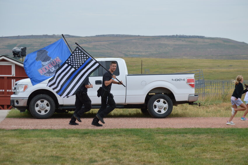 Deputy John Gray, a school resource officer who is partnered with therapy dog Rex, held a flag while running during the 2023 RexRun on Aug. 26.